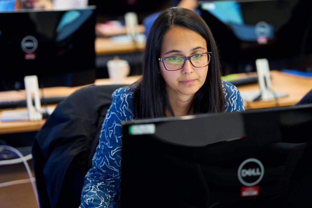 A course participant with medium length brown hair, and wearing glasses. They are seated in front of a desktop computer screen. 