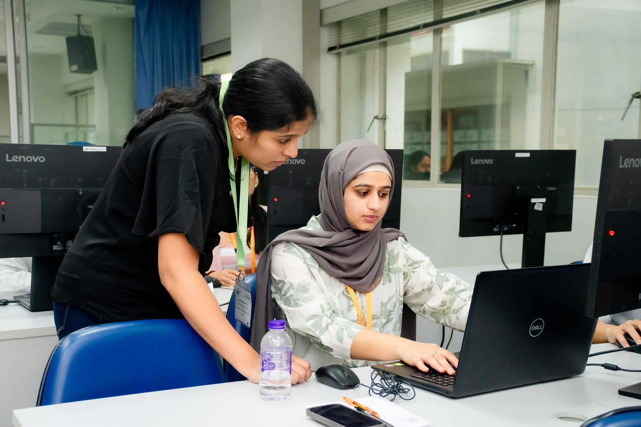 A course participant and trainer in a computational session classroom. They are both looking at a laptop on a desk. 