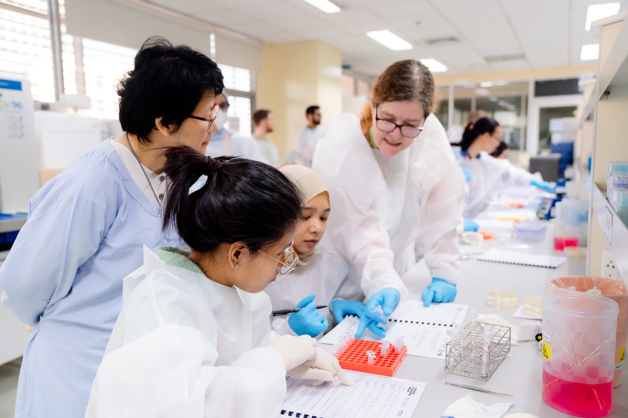 A group of course participants in a training laboratory, looking at the training manual, accompanied by one of the course instructors. 