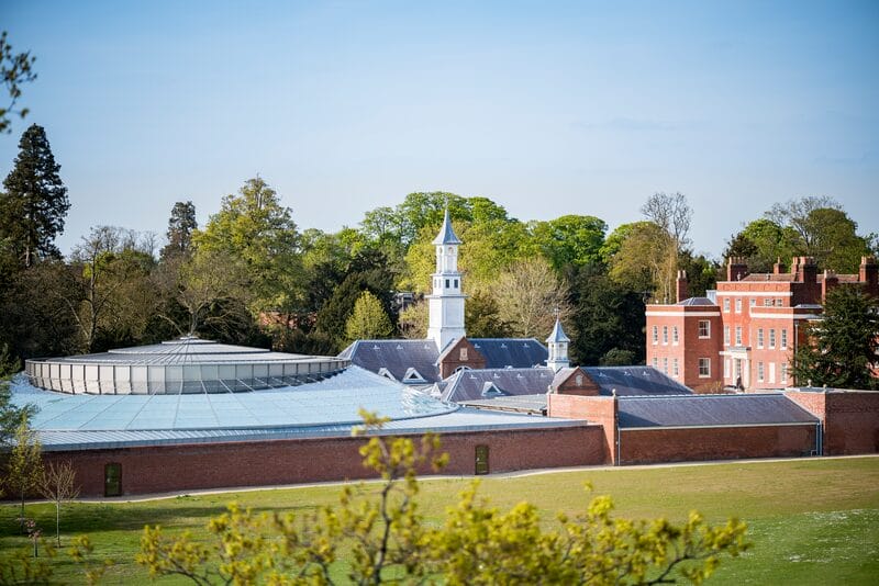 A wide angle photo of Hinxton Hall Conference Centre in the daytime. Lush green trees are in the background.