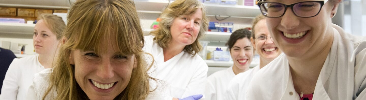 A group of teachers in a lab, wearing lab coats - they are smiling.